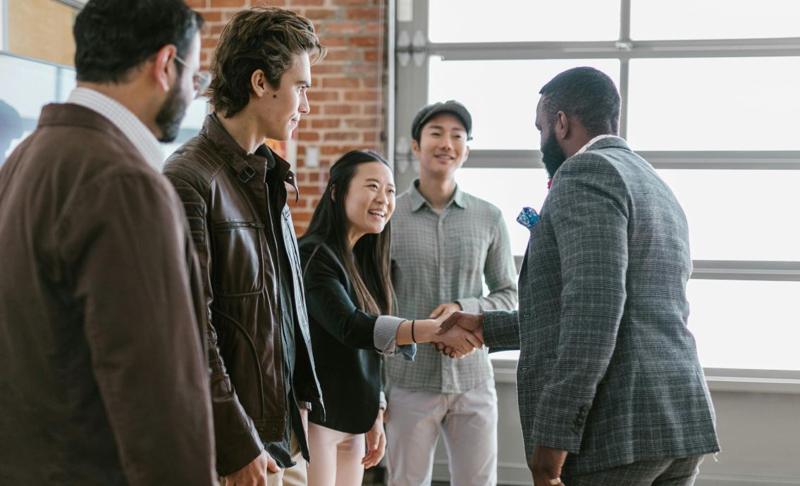 A diverse group of business professionals engaging in a handshake and discussion in a modern office space.